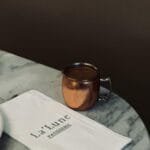 Copper mug on marble table with La'Lune patisserie napkin, elegant cafe ambiance.