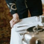 A hotel staff member in uniform setting up a luxurious room service tray.